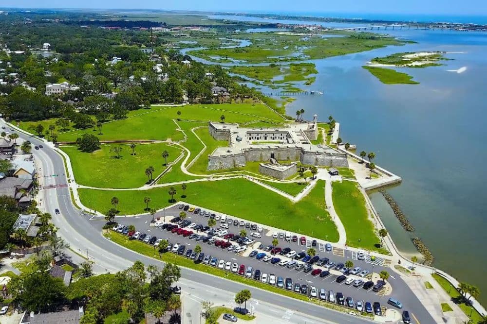 Aerial view of a historic fort surrounded by green lawns, a parking lot, and waterways.