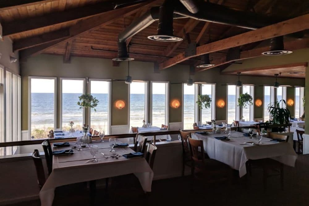 A spacious restaurant interior with ocean views and elegantly set tables.