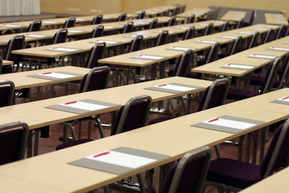 A row of neatly arranged tables with sheets of paper and pens, ready for an event.
