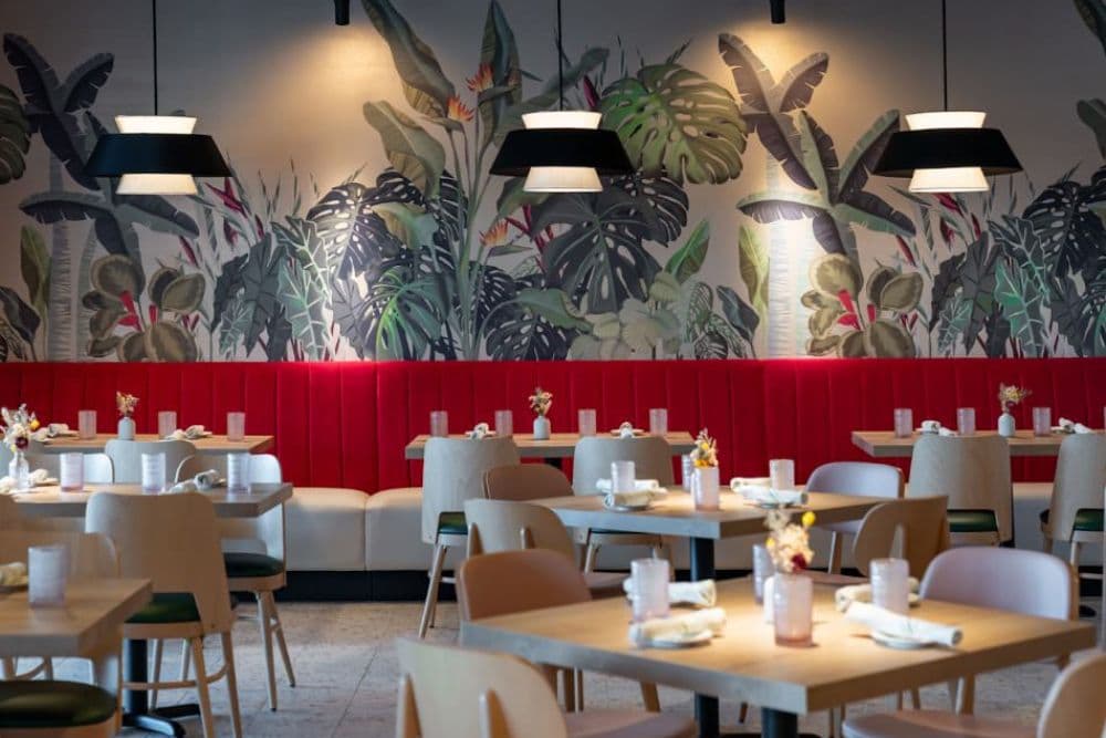 Modern restaurant interior featuring wooden tables, colorful seating, and a vibrant tropical mural.