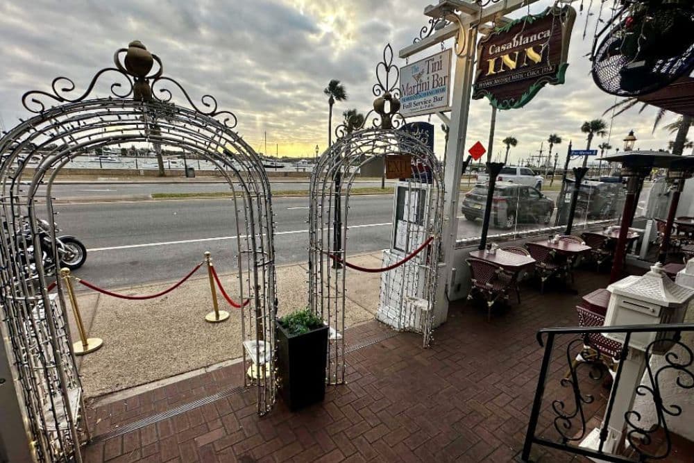 Entrance to a restaurant with decorative arches, a view of the street, and outdoor seating.