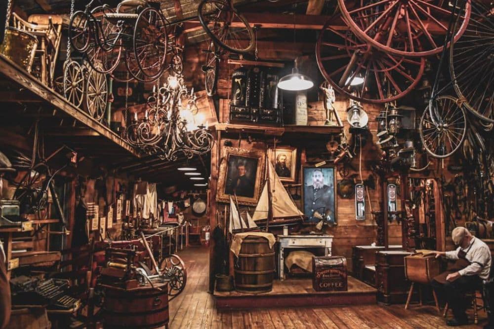 A vintage-themed room filled with various antiques, including bicycles, a chandelier, and old portraits.