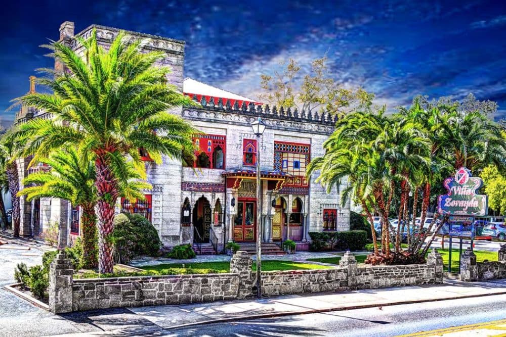 A colorful historical building surrounded by palm trees and a stone wall.