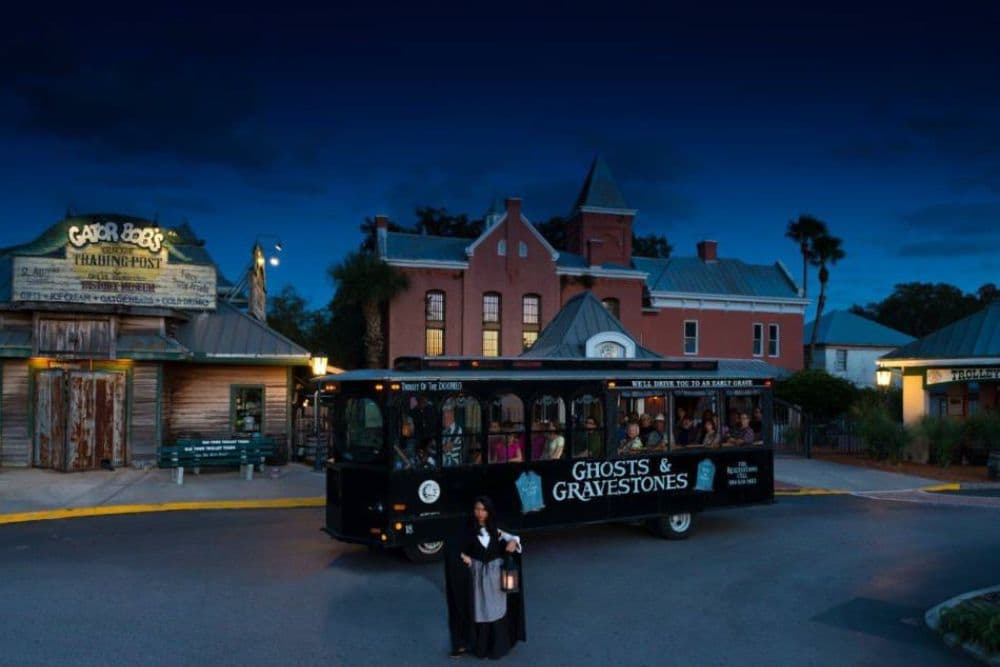 A ghost tour trolley stops in front of historic buildings at dusk, with a tour guide holding a lantern.