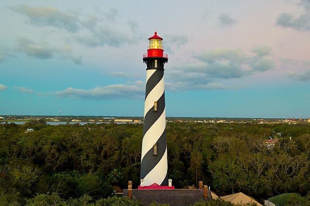 A tall black and white striped lighthouse stands amidst a green landscape under a cloudy sky.