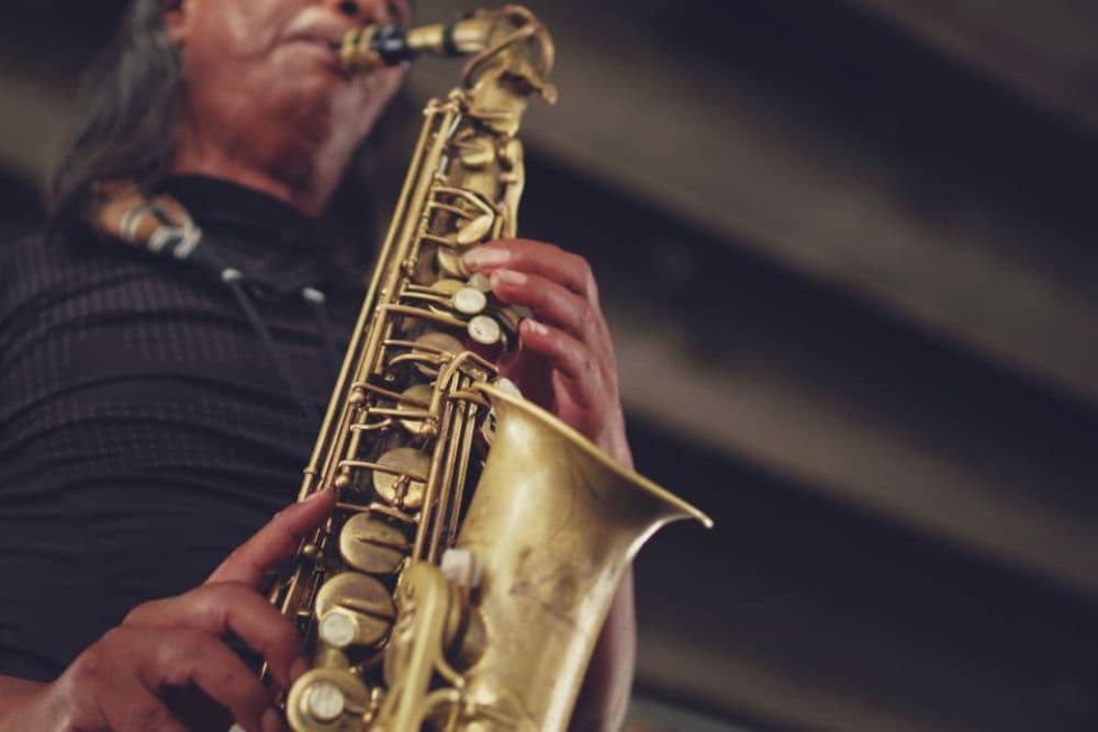 A musician plays a saxophone underneath an urban setting.