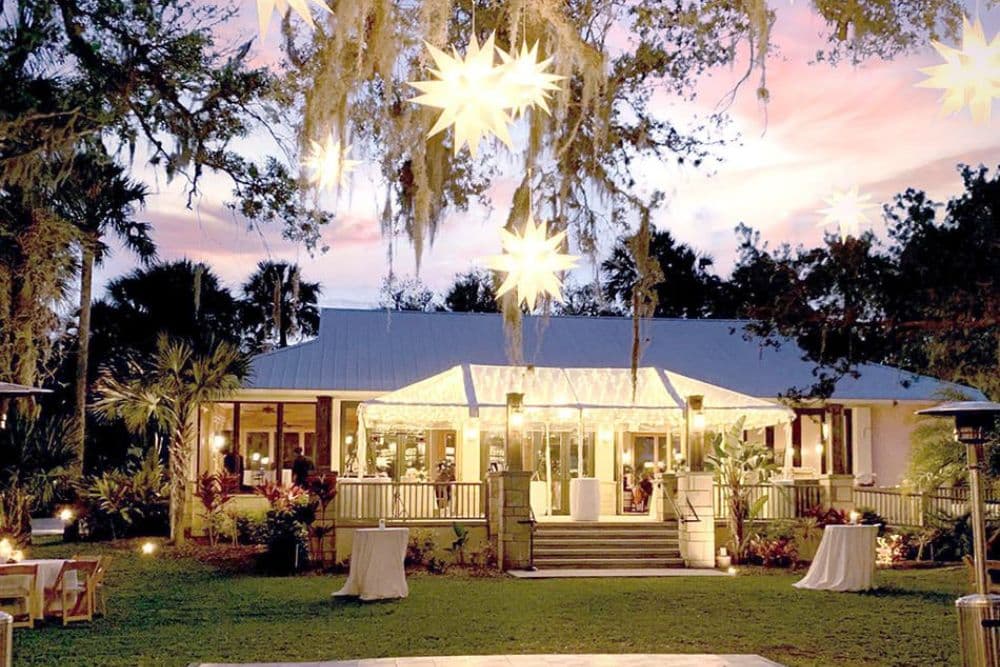 A charming outdoor venue with string lights and a welcoming entrance surrounded by lush greenery at sunset.