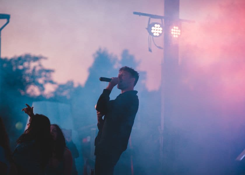 musician singing into microphone on stage with colorful lights and smoke during outdoor concert musician singing into microphone on stage with colorful lights and smoke during outdoor concert
