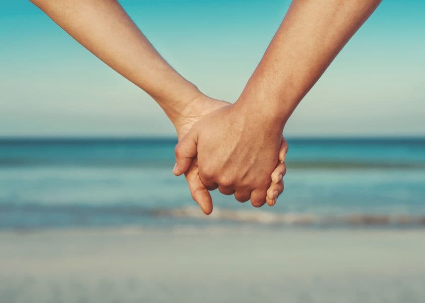Couple holding hands on the beach with the ocean in the background. Couple holding hands on the beach with the ocean in the background.