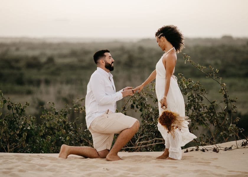man kneeling to propose to a woman on a sandy beach during a quiet outdoor moment man kneeling to propose to a woman on a sandy beach during a quiet outdoor moment